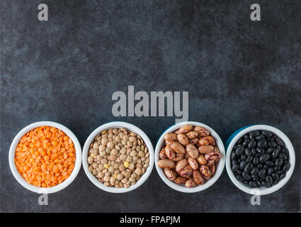 Red and brown lentils, heirloom beans, and black turtle beans on dark grungy surface. Top view with copy space. Stock Photo