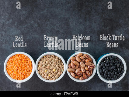 Red and brown lentils, heirloom beans, and black turtle beans on dark grungy surface. with labels. Top view horizontal image wit Stock Photo