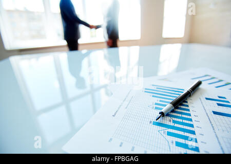 Business documents with charts on the table with business people in the background Stock Photo