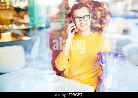 Young man in glasses talking on the mobile phone while sitting in cafe Stock Photo