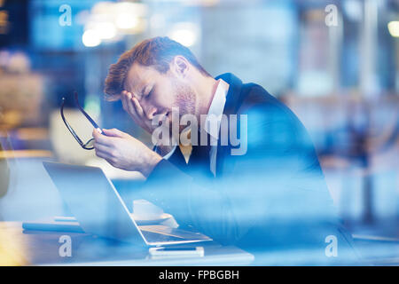 Tired young businessman using a laptop while working in cafe Stock Photo