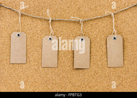 Vintage grunge empty tags hanging on rope string over cork board texture background, available copy space Stock Photo