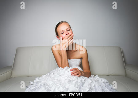 Super tired gorgeous bride sitting on a sofa after a long wedding day, yawning Stock Photo