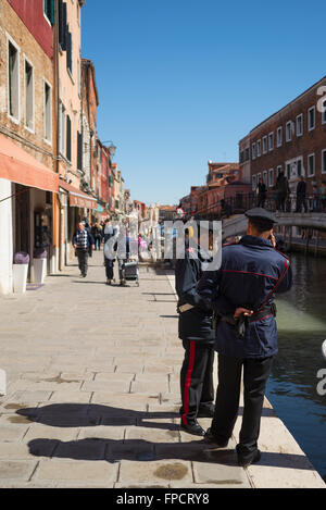 One policemen waiting and one policemen doing a call on a bright spring morning at a canal on Murano island,Venice,Italy Stock Photo