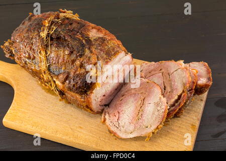 Roasted rolled pork meat on a cutting board on a black table Stock Photo