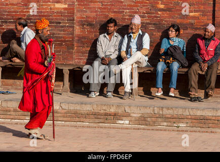 Nepal, Patan.  A Hindu Sadhu (Holy Man) Walks Past Men and One Woman Resting on Bench in Durbar Square. Stock Photo