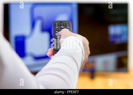Closeup on woman hand holding remote control  and surfing internet on television. Focus on the remote control. Stock Photo