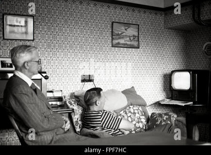 1950s, historical, a father and son siting in a front room watching a small television set of the era, the elderly man smoking a pipe, a common thing for men of a certain age to do at this time. Stock Photo