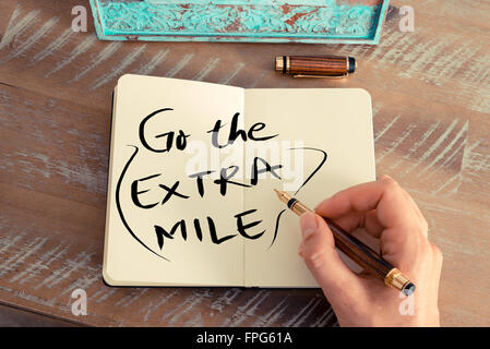 Retro effect and toned image of a woman hand writing a note with a fountain pen on a notebook. Handwritten text GO THE EXTRA MILE, business success concept Stock Photo