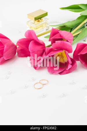 bouquet of red tulips, wedding rings, perfume and bead lying on a white background Stock Photo