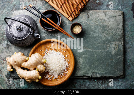 Raw white rice, green tea teapot, soy sauce and sushi chopsticks on gray stone slate background Stock Photo