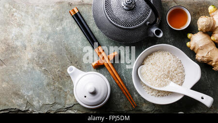 Raw white rice, green tea teapot, soy sauce and sushi chopsticks on gray stone slate background Stock Photo