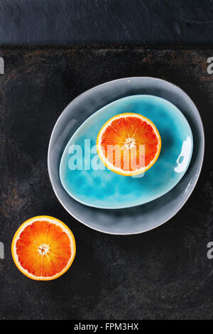 Sliced Sicilian Blood orange fruit on bright turquoise and gray ceramic plates over black background. Flat lay Stock Photo