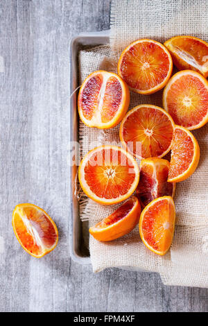 Sliced Sicilian Blood oranges fruits in aluminum tray with white sackcloth over gray wooden background. Top view Stock Photo