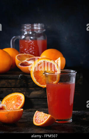 Sliced and whole Sicilian Blood oranges and glass of fresh red orange juice over old wooden table. Dark rustic style. Stock Photo
