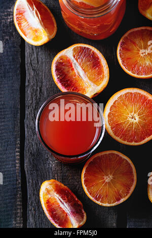 Sliced Sicilian Blood oranges in turquoise ceramic plate and glass of fresh red orange juice over old wooden table. Dark rustic Stock Photo