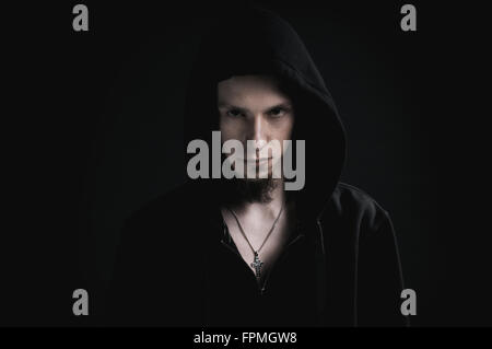 Young bearded man hooded portrait on black background, straightfaced person looking to the camera with serious focused eyes Stock Photo