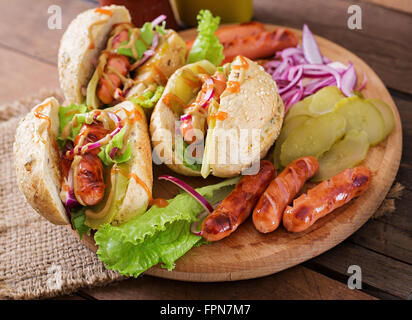 Hot dog - sandwich with pickles, red onions and lettuce on wooden background. Stock Photo