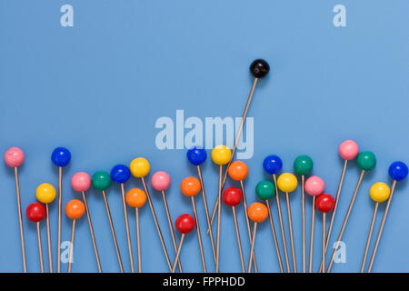 Colourful berry pins on blue background with odd black pin sticking out showing concept of standing out from the crowd Stock Photo