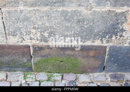 Old stone wall and cobblestone street with moss growing Stock Photo