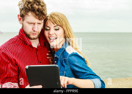 Modern technology devices and tourism concept. Young couple outdoor against sea water with tablet enjoying summer holidays Stock Photo