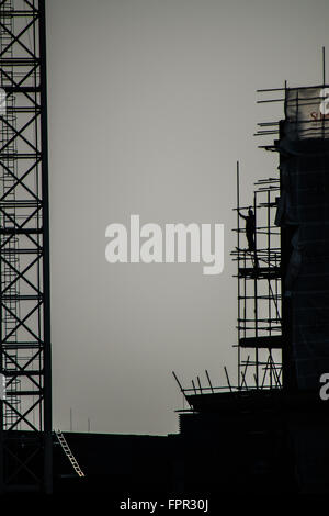 A scaffolder works at height erecting scaffolding on the south bank of the Thames near Battersea. Scaffold. Silhouette. Construction Stock Photo