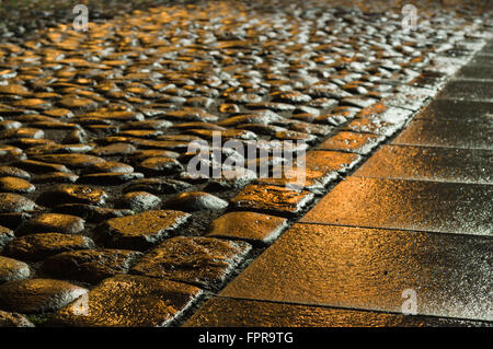 Wet shiny block pavement at night in the orange light of lanterns Stock Photo