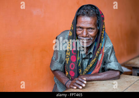 Smiling indian man sitting beside orange wall Stock Photo