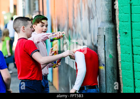 Belfast, Northern Ireland. 17 Mar 2016 - Two older boys bully a younger boy by spraying his hair with green spray paint.