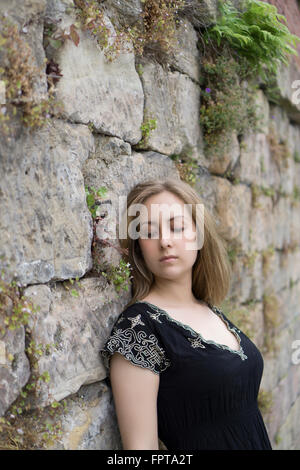Sad young woman leaning against the wall outdoors Stock Photo