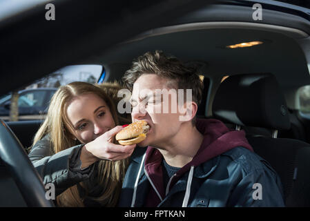 Young couple sitting in a car and she is feeding him a burger, Munich, Bavaria, Germany Stock Photo