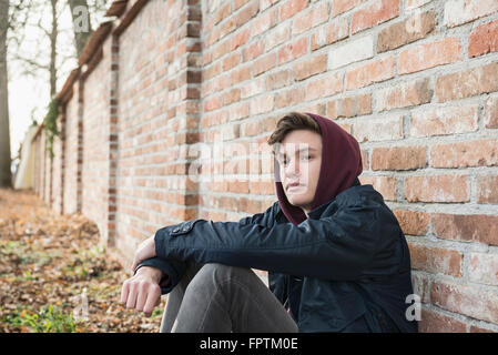 Young man sitting against brick wall and thinking, Munich, Bavaria, Germany Stock Photo