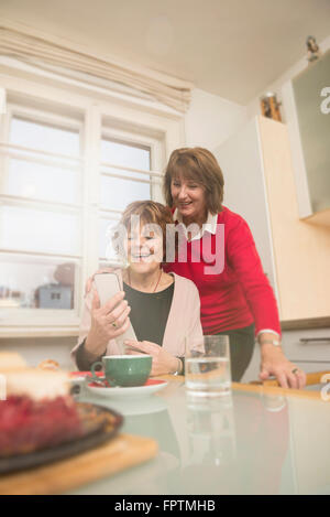 Two senior women using smart phone in kitchen, Munich, Bavaria, Germany Stock Photo