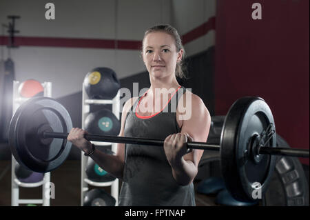 Young woman in the gym lifting barbell rod for bicep exercise, Bavaria, Germany Stock Photo