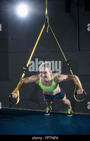 Sportive woman doing press-ups with TRX belt in health club, Bavaria, Germany Stock Photo