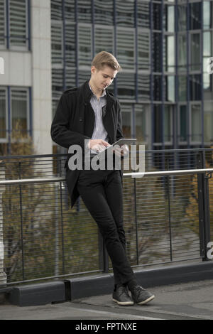 Teenage businessman waiting for someone and using digital tablet against railing, Bavaria, Germany Stock Photo