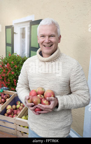 Portrait of a mature man holding apples in his hands in front of wholefood shop and smiling, Bavaria, Germany Stock Photo