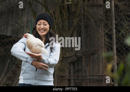 Farmer woman with white chicken bird and smiling in farm, Bavaria, Germany Stock Photo