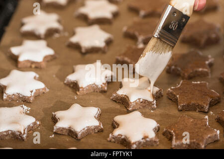 Close-up of a woman icing star shape cinnamon with basting brush, Munich, Bavaria, Germany Stock Photo