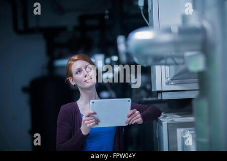 Young female engineer using a digital tablet and thinking in an industrial plant, Baden-Württemberg, Germany Stock Photo