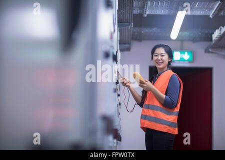 Young female engineer examining control panel with multimeter in an industrial plant, Baden-Württemberg, Germany Stock Photo