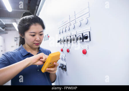 Young female engineer examining control panel with multimeter in an industrial plant, Baden-Württemberg, Germany Stock Photo