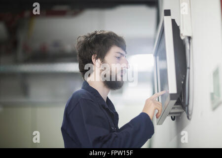 Young male engineer working on touchscreen computer monitor in an industrial plant, Baden-Württemberg, Germany Stock Photo