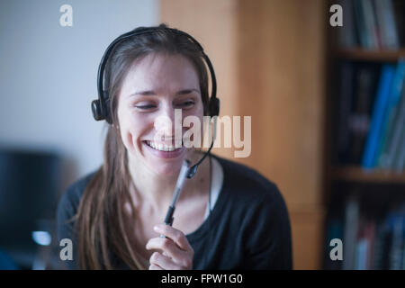 Young woman smiling and talking on headset, Freiburg im Breisgau, Baden-Württemberg, Germany Stock Photo