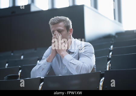 Tensed young man sitting in lecture hall by covering his face, Freiburg im Breisgau, Baden-Württemberg, Germany Stock Photo