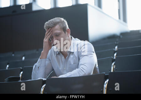 Young man sitting with tension in lecture hall with head in hands, Freiburg im Breisgau, Baden-Württemberg, Germany Stock Photo
