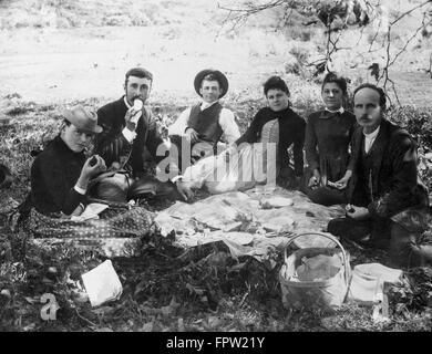 1890s 1900s GROUP OF SIX PEOPLE SITTING AROUND AN OUTDOOR PICNIC SPREAD ON THE GROUND LOOKING AT CAMERA Stock Photo