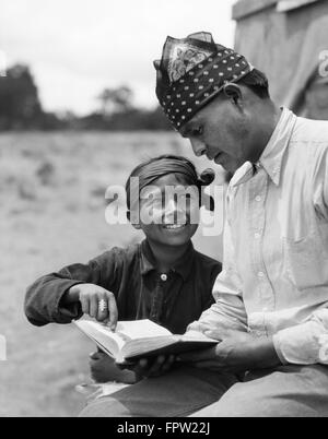 1930s SMILING NATIVE AMERICAN BOY NAVAJO POINTING & READING BOOK WITH MAN FATHER TEACHER Stock Photo