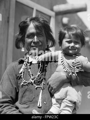 1930s SMILING NATIVE AMERICAN MAN LOOKING AT CAMERA HOLDING HIS SON COCHITI PUEBLO NEW MEXICO USA Stock Photo