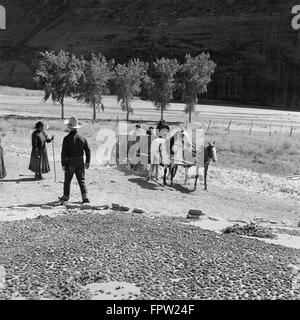 1930s GROUP OF NATIVE AMERICAN NAVAJO INDIANS DRYING CORN WATCHING WOMAN CHILDREN RIDING IN CART WAGON DRAWN BY TWO HORSES Stock Photo